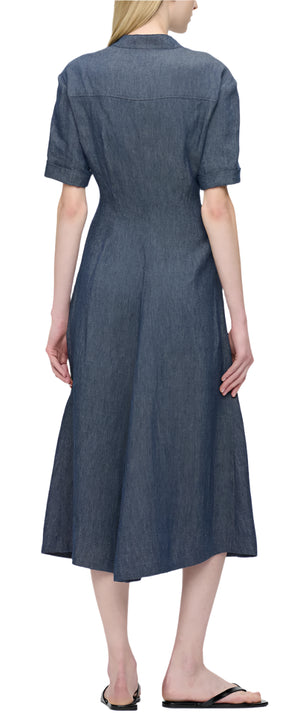 A person is seen from behind wearing a stylish Callas Milano Noor Dress in denim, featuring short sleeves and a comfortable fit and flare silhouette, paired with black sandals.