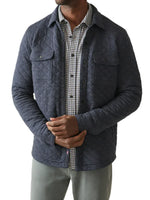 A person wearing the Faherty Epic Quilted Fleece in navy over a relaxed-fit shirt and gray pants stands against a plain background.