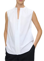 Wearing the Olympia Sleeveless Top by Callas Milano in white, paired with black pants and hands in pockets, exudes a modernist appeal.