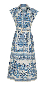 The Octavia Dress by Cara Cara features a crisp white design with blue ornate floral patterns, short sleeves, a button-up front, and a matching fabric belt with a circular buckle.