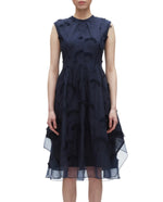 A woman wears the 3.1 Phillip Lim Fil Coupé Midi Dress, a dark navy, knee-length sleeveless dress with a high neckline and textured floral embroidery.