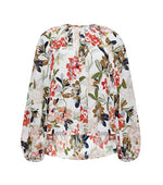 The Lottie Top by Adam Lippes is a long-sleeved, loose-fit blouse crafted from crepe de chine, featuring an ivory floral pattern in red, pink, green, and navy on white.