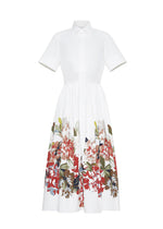 The Attacher Dress by Adam Lippes is a white short-sleeve, collared shirt dress in Italian cotton poplin, with a fitted waist and full skirt, featuring a red, green, and brown floral motif print along the bottom half.