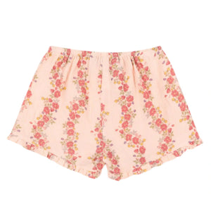 Konges Slojd Baby Girls' and Girls' Coco Shorts in light pink with a red and green floral pattern, made from breathable muslin, feature an elastic waistband and ruffled leg openings, shown laid flat on a white background.