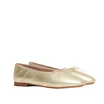 The Dream Ballerina by Mansur Gavriel is a pair of gold Italian lambskin flats with a knotted bow, low wooden heels, and a soft rounded toe, displayed on a white background.
