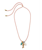 The Minnow Necklace by Lizzie Fortunato features a red and white braided cord with gold-tone ends, adorned with a turquoise stone, gold fish, pearl-like charm, and a delicate gold-plated bead for elegance.