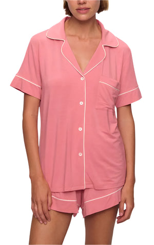 A person wearing the Eberjey Gisele Relaxed Short PJ Set, featuring a pink short-sleeve button-up top with white piping and matching shorts for a comfortable fit.