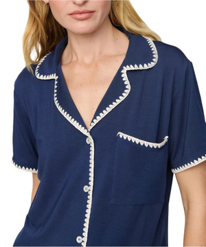 A woman wears the Eberjey Frida Relaxed Short PJ Set—featuring a navy, relaxed-fit short-sleeve top with white scalloped trim, chest pocket, and button-down front.