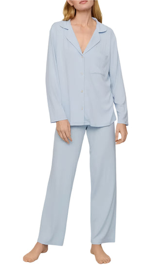 A person wears the Eberjey Gisele Rib Long PJ Set, featuring a light blue button-down top and matching loose-fitting pants with an elastic waistband, while standing barefoot.
