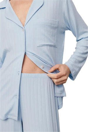 A person wears the Eberjey Gisele Rib Long PJ Set—a light blue, ribbed button-down top and pants—holding the shirt slightly open at the waist.