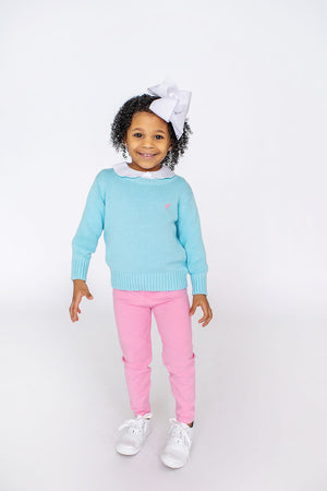 A smiling child wearing a light blue sweater, Hamptons Hot Pink pants, white sneakers, and The Beaufort Bonnet Company Girls' Mitzy Sue Slacks stands against a white background.