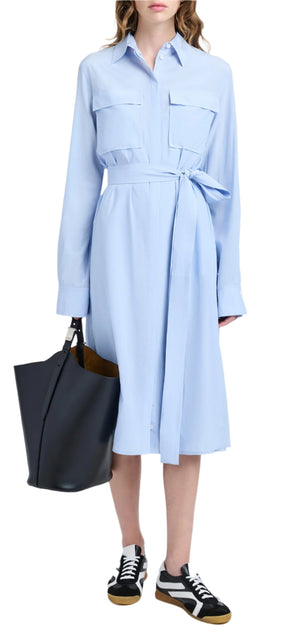 A woman wearing the Proenza Schouler McKenna Dress, featuring a concealed button front and self-tie waist belt, is carrying a black tote bag and sporting black and white sneakers.