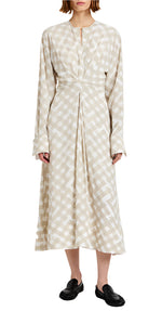 A person wears the Proenza Schouler Keria Printed Crepe De Chine Dress, a long-sleeved beige and white checkered midi, with black slip-on shoes, standing against a white background.