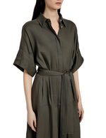 A woman wearing the Scottie Dress by Proenza Schouler, an olive green collared shirt dress in Eco Stretch Linen with short sleeves and a self-tie waist belt.