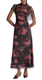 A person wears the Lela Rose Draped Bodice A Line Dress, a long dark overlay with translucent short sleeves and a red floral pattern, paired with red low-heeled shoes.