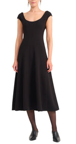 A woman wears the Staud Charlotte Dress—black, short-sleeve, scoop-neck, midi-length—paired with black tights and black shoes.
