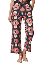 Person sporting the Jolie Pant by Figue, showcasing abstract shapes in pink, black, and white with a drawstring waistband and front pockets. The look is elegantly finished with white high-heeled sandals.