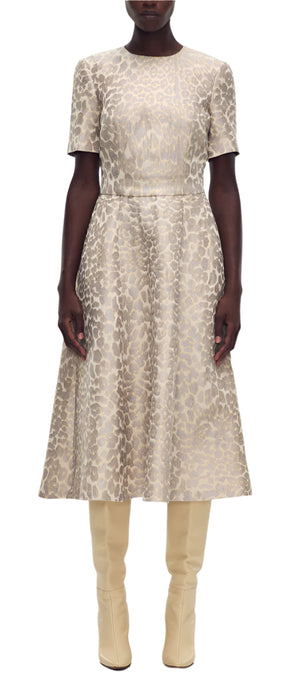 A person in an Eloise Dress Leopard Jacquard by Adam Lippes and beige knee-high boots stands confidently against a plain white backdrop.