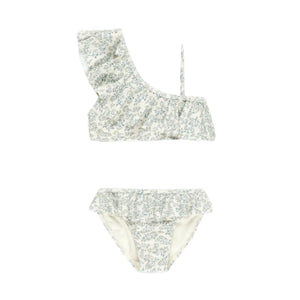 The Rylee & Cru Girls' Skirted Bikini features a white base with light blue florals, an asymmetrical ruffle top, matching ruffled skirted bottoms, and UPF 50+ sun protection—perfect for stylish days by the pool or beach.