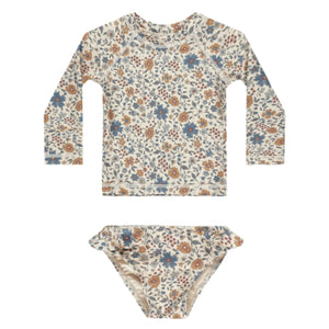 The Rylee & Cru Baby Girls' and Girl's Maryn Rashguard Set features a blue and brown floral print on off-white, with long sleeves, matching bikini bottoms, and UPF 50+ protection, shown laid flat on a white surface.