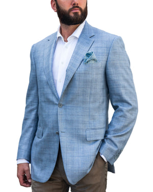 A man wears the Canali Sky Blue Fine Plaid Blazer with a modern fit, paired with a white dress shirt, tan pants, and a blue patterned pocket square accenting the wool blazer. One hand is in his pocket.