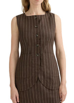A woman wears the Emma Pinstripe Vest by POSSE—a sleeveless, brown pinstripe vest with front buttons, two large front pockets, and a classic silhouette, crafted from premium linen.