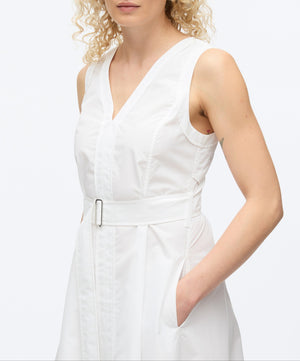 A woman models the 3.1 Phillip Lim Crisscross Back Midi Dress, a sleeveless white V-neck design with a belted waist and A-line skirt, standing with one hand in her pocket against a plain background.