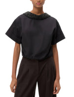 A person wearing the TWP Forever and Always Crystal Collar Shirt with short sleeves and dark high-waisted pants stands against a plain background.