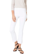 The person is wearing Ann Mashburn's Faye Flare Cropped Stretch Twill Pants in white, a striped top, and black sandals while standing against a plain background.