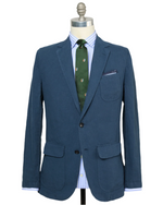 The Sid Mashburn Butcher Jacket is showcased on a mannequin, paired with a blue and white striped shirt and a patterned green tie.