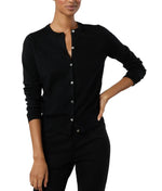 A woman stands with one hand on her hip, wearing black pants and the Ann Mashburn Rosie Cotton Silk Cardigan, a black long-sleeve women's sweater.