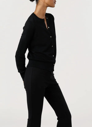 A person wears the Ann Mashburn Rosie Cotton Silk Cardigan in black with black pants, standing sideways against a plain light background, arms relaxed behind their back.