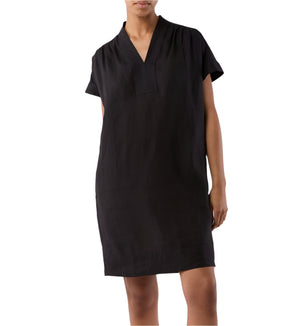 A person models the Ann Mashburn Libby Dress, a short-sleeve, knee-length black V-neck design, standing against a plain background.