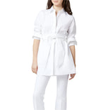 A woman wears the Gabrielle Tie Tunic by Ann Mashburn—a white Italian poplin top with a waist tie and rolled sleeves—paired with matching white pants, standing against a plain background.