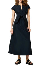 Wearing the chic Gigi Dress by Ann Mashburn—a long, dark A-line design with short sleeves and a front tie belt—creates an elegant look in nylon faille, perfectly complemented with black sandals.