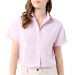 A woman shown from shoulders to hips wears the Agnes Shirt by Ann Mashburn, a light pink Italian chambray short-sleeve button-up with Trocas shell buttons, paired with light-colored pants.