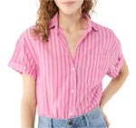 Someone is wearing the Ann Mashburn Agnes Shirt—a pink and red vertically striped, oversized short-sleeve button-up with Trocas shell buttons—paired with light blue jeans.