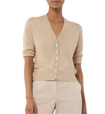 A person models the Ann Mashburn Rosie Cardigan—a beige V-neck, button-up sweater with rolled sleeves—paired with matching beige pants, shown from shoulders to hips.