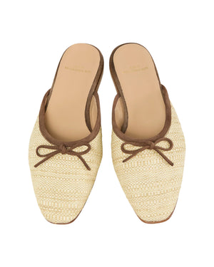 The Ann Mashburn Joy Basketweave Mule features beige slip-on flats with an almond-shaped toe, brown trim, and a small bow detail.