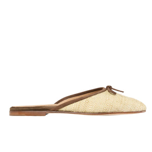 The Ann Mashburn Joy Basketweave Mule is a tan and brown slip-on with an almond-shaped toe box, flat sole, and a small bow detail on top.