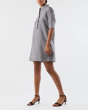 A woman wears the Ann Mashburn Elbow Sleeve Frill Dress, a feminine knee-length black-and-white checkered piece with a standing collar and front buttons, paired with black strappy heels and a neatly finished hem.