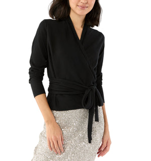A woman wears the Ann Mashburn Mika Cashmere Wrap Sweater in black, styled with a waist tie and paired with a silver sequin skirt, standing against a white background.
