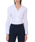 A person models a chic silhouette against a minimal backdrop, wearing Callas Milano's Savile Top, a white cotton poplin long sleeve button-up shirt, paired with dark pants.
