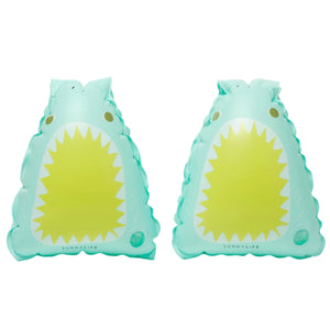 The Float Bands Salty the Shark Aqua by Sunnylife, featuring a vibrant green cartoon shark with a wide yellow mouth and white teeth, are ideal swimming accessories to boost children's confidence in the water.