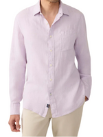 A man wears the Laguna Linen Shirt by Faherty, a lightweight, light pink button-up with long sleeves, paired with beige pants and his left hand in his pocket.