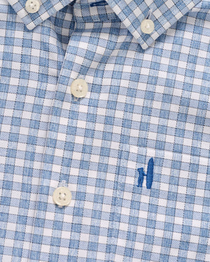 Close-up of the Johnnie-O Boys' Performance Jr. Button Up Shirt Westwood Print, featuring a blue and white plaid pattern, Tweener® button, white buttons, and a small blue embroidered chest design.