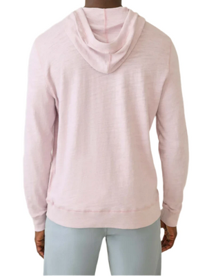 The individual is seen from behind, wearing the Faherty Sunwashed Slub Hoodie in light pink, made from American-grown cotton, paired with light gray pants, all set against a plain white backdrop to emphasize the relaxed fit of their outfit.