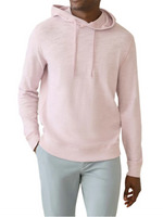 A person in a relaxing Faherty Sunwashed Slub Hoodie in light pink and relaxed-fit light gray pants stands casually with one hand in their pocket.