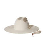 The Palmer Hat by Janessa Leone is a wide-brimmed, off-white palm straw hat with a rounded crown and organic cotton ties with regenerative leather aglets, shown against a plain white background.