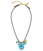 The Shibori Flower Necklace by Lizzie Fortunato features a black leather cord, a large blue floral pendant, imitation turquoise and white beads, gold charms, rhodolite stone accents, and an adjustable gold clasp.
